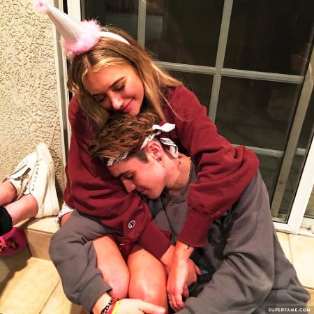 stassie wearing a birthday hat and hugging sam from behind 